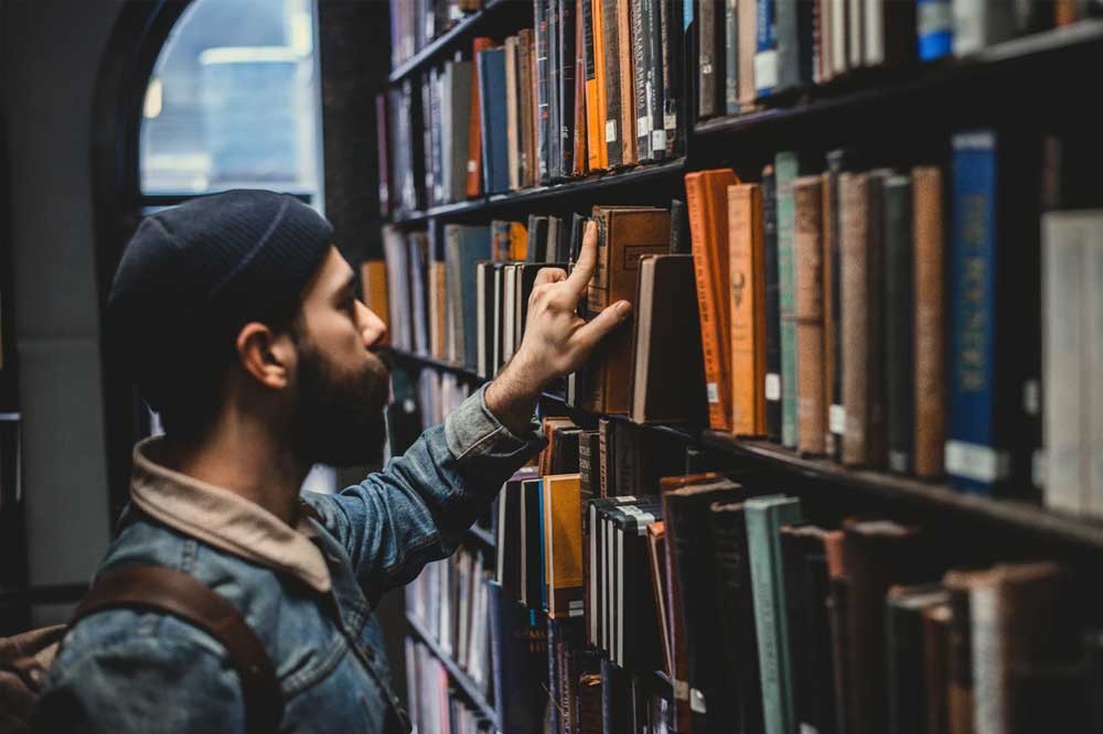 student stands in front of bookshelf