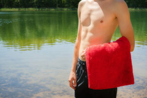 Junger Mann mit rotem Handtuch vor Schwimmteich